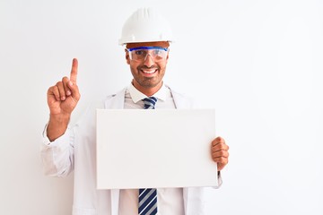 Young chemist man wearing security helmet holding signboard over isolated background surprised with an idea or question pointing finger with happy face, number one