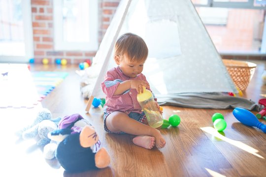 Adorable toddler holding feeding bottle around lots of toys at kindergarten