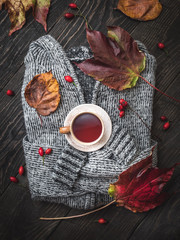 Cup of rose hip tea on grey knitted sweater. Colorful autumn lea