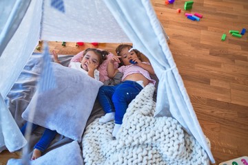 Adorable toddlers lying down over blanket inside tipi smiling at kindergarten