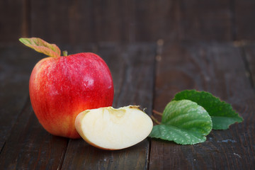 Fresh red apple with leaves on wooden background. Organic apple, one cut. Sweet, healthy fruit.