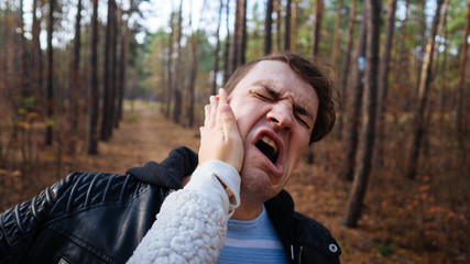 A woman's hand hits a man's face in the autumn forest. An emotional male is getting slapped in face, while shouting with closed eyes in a fear.