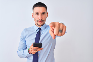 Young handsome business man using smartphone over isolated background pointing with finger to the camera and to you, hand sign, positive and confident gesture from the front