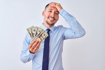 Young handsome business man holding a bunch of bank notes dollars over isolated background stressed with hand on head, shocked with shame and surprise face, angry and frustrated. Fear and upset 