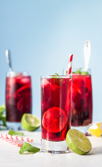 Iced hibiscus tea (karkade, red sorrel, Agua de flor de Jamaica) or lemonade with raspberries, blackberries, mint and citrus on a light grey background. 