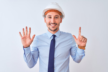 Young business man wearing contractor safety helmet over isolated background showing and pointing up with fingers number seven while smiling confident and happy.