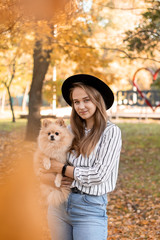 Happy female owner with her dog on hands, arms. Young woman hugging her miniature fluffy Pomeranian Spitz puppy outdoor in an autumn park. People love their pet concept
