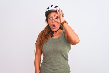 Middle age mature cyclist woman wearing safety helmet over isolated background doing ok gesture shocked with surprised face, eye looking through fingers. Unbelieving expression.