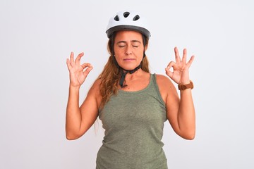 Middle age mature cyclist woman wearing safety helmet over isolated background relaxed and smiling with eyes closed doing meditation gesture with fingers. Yoga concept.