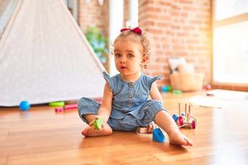 Beautiful caucasian infant playing with toys at colorful playroom. Happy and playful with wooden train pieces at kindergarten.