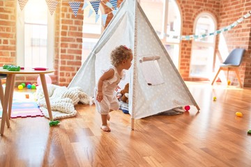 Beautiful caucasian infant playing with toys at colorful playroom. Happy and playful with indian tent at kindergarten.