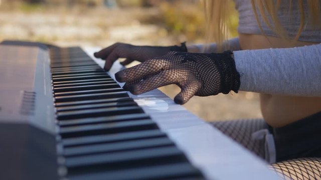 Close-up of girl in black mesh gloves playing on synthesizer in autumn Park.