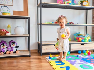 Beautiful caucasian infant playing with toys at colorful playroom. Happy and playful wth colorful balls at kindergarten.