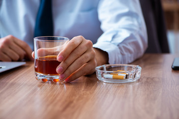 Male employee drinking alcohol and smoking cigarettes at workpla