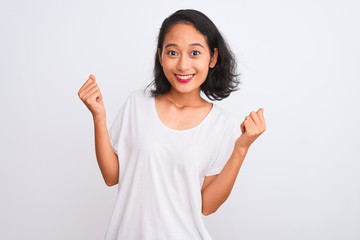 Obraz na płótnie Canvas Young chinese woman wearing casual t-shirt standing over isolated white background celebrating surprised and amazed for success with arms raised and open eyes. Winner concept.