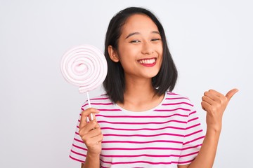 Young beautiful chinese woman eating lollipop standing over isolated white background happy with big smile doing ok sign, thumb up with fingers, excellent sign