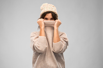 winter season and people concept - happy young woman in knitted hat covering face with warm sweater...