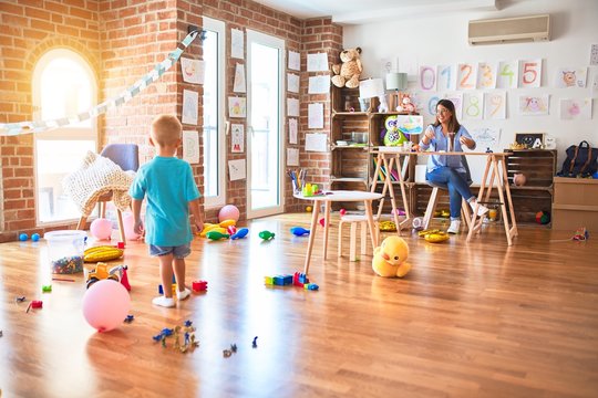 Young caucasian child playing at playschool with teacher. Young woman sitting on the desk of the classroom