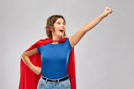 women's power and people concept - happy woman in red superhero cape making flying pose over grey background