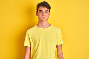 Fototapeta premium Teenager boy wearing yellow t-shirt over isolated background puffing cheeks with funny face. Mouth inflated with air, crazy expression.