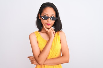 Young beautiful chinese woman wearing thug life sunglasses over isolated white background with hand on chin thinking about question, pensive expression. Smiling with thoughtful face. Doubt concept.