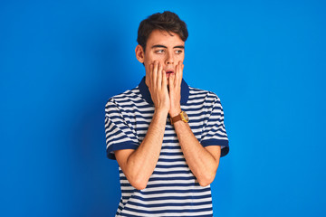 Teenager boy wearing casual t-shirt standing over blue isolated background Tired hands covering...
