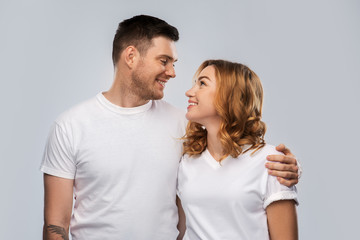 relationships and people concept - portrait of happy couple in white t-shirts looking at each other over grey background