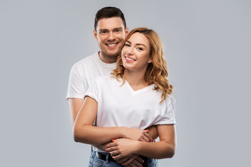 Naklejka premium relationships and people concept - portrait of happy couple in white t-shirts over grey background