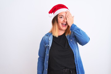 Young beautiful woman wearing Christmas Santa hat standing over isolated white background covering one eye with hand, confident smile on face and surprise emotion.