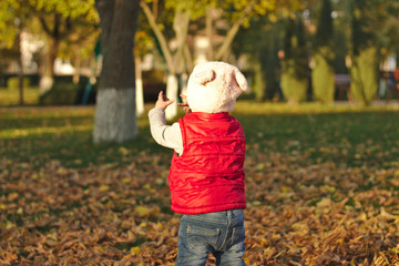 A merry child scatters an armful of yellow fallen leaves. Sunny sunset in autumn park outdoors