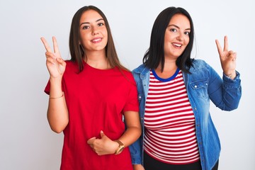 Young beautiful women wearing casual clothes standing over isolated white background smiling looking to the camera showing fingers doing victory sign. Number two.