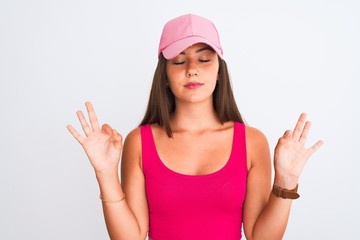 Obraz na płótnie Canvas Young beautiful girl wearing pink casual t-shirt and cap over isolated white background relax and smiling with eyes closed doing meditation gesture with fingers. Yoga concept.