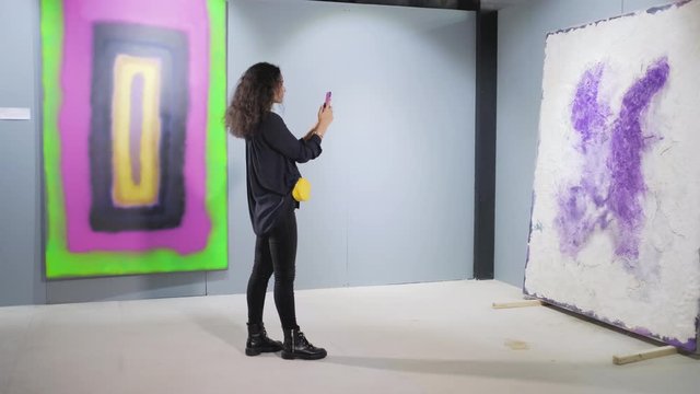 Woman art lover taking photos in picture gallery