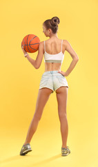 Sexy Girl wearing short shorts holding a basketball on yellow background