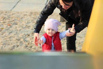 Mom helps the child climb the iron slide