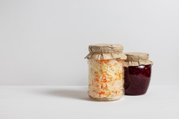 Homemade sauerkraut with carrots and cabbage salad with beets in a glass jar on a white wooden background. Fermented food. Copy space