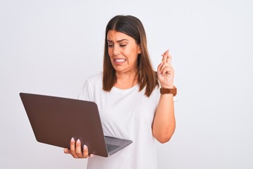 Beautiful young woman working using computer laptop over white background gesturing finger crossed smiling with hope and eyes closed. Luck and superstitious concept.