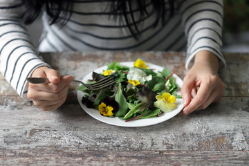 Selective focus. Girl is eating salad. Healthy salad with flowers on a plate. Diet concept.