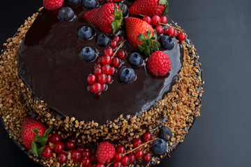 Close-up. Angular plane. Homemade Chocolate Cake. Chocolate bavaroise and chocolate topping garnished with strawberries, red currants and blueberries. Brown background.