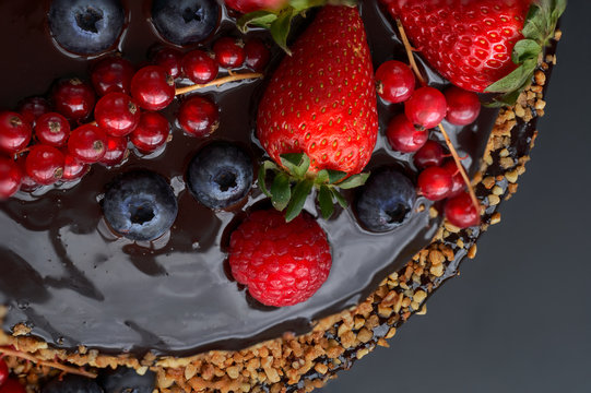 Partail view. Homemade Chocolate Cake. Chocolate bavaroise with chocolate topping. Garnished with red currants, strawberries, blueberries and chopped and toasted almonds. Dark background.