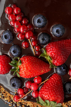 Partail view. Homemade Chocolate Cake. Chocolate bavaroise with chocolate topping. Garnished with red currants, strawberries, blueberries and chopped and toasted almonds. Dark background.