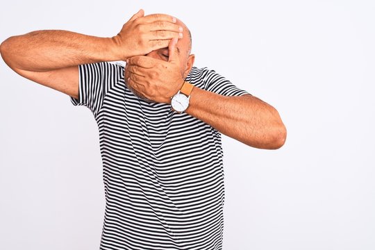 Middle age handsome man wearing striped navy t-shirt over isolated white background Covering eyes and mouth with hands, surprised and shocked. Hiding emotion