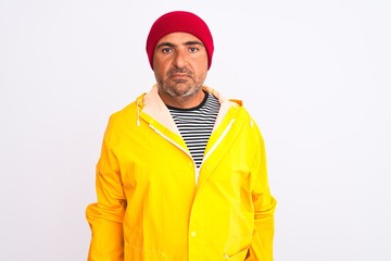 Middle age man wearing rain coat and woolen hat standing over isolated white background Relaxed with serious expression on face. Simple and natural looking at the camera.