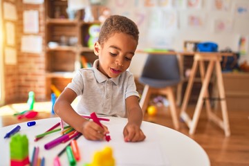 Beautiful african american toddler drawing using paper and marker pen smiling at kindergarten