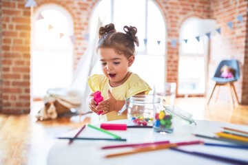 Beautiful toddler playing with wooden building blocks on the table at kindergarten