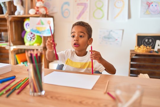Beautiful african american toddler sitting drawing using paper and pencils on desk at kindergarten