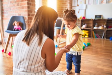 Young beautiful teacher and toddler playing with small building blocks toy at kindergarten