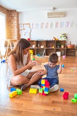 Young beautiful teacher and toddler playing with building blocks toy at kindergarten