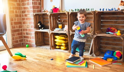 Beautiful toddler standing playing with colorful plastic cups at kindergarten