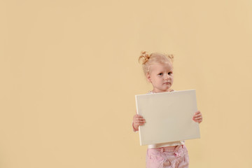 Giggles happy baby girl with blond hair. Confused little girl holding a poster for your information. on a bright yellow background.Copy space